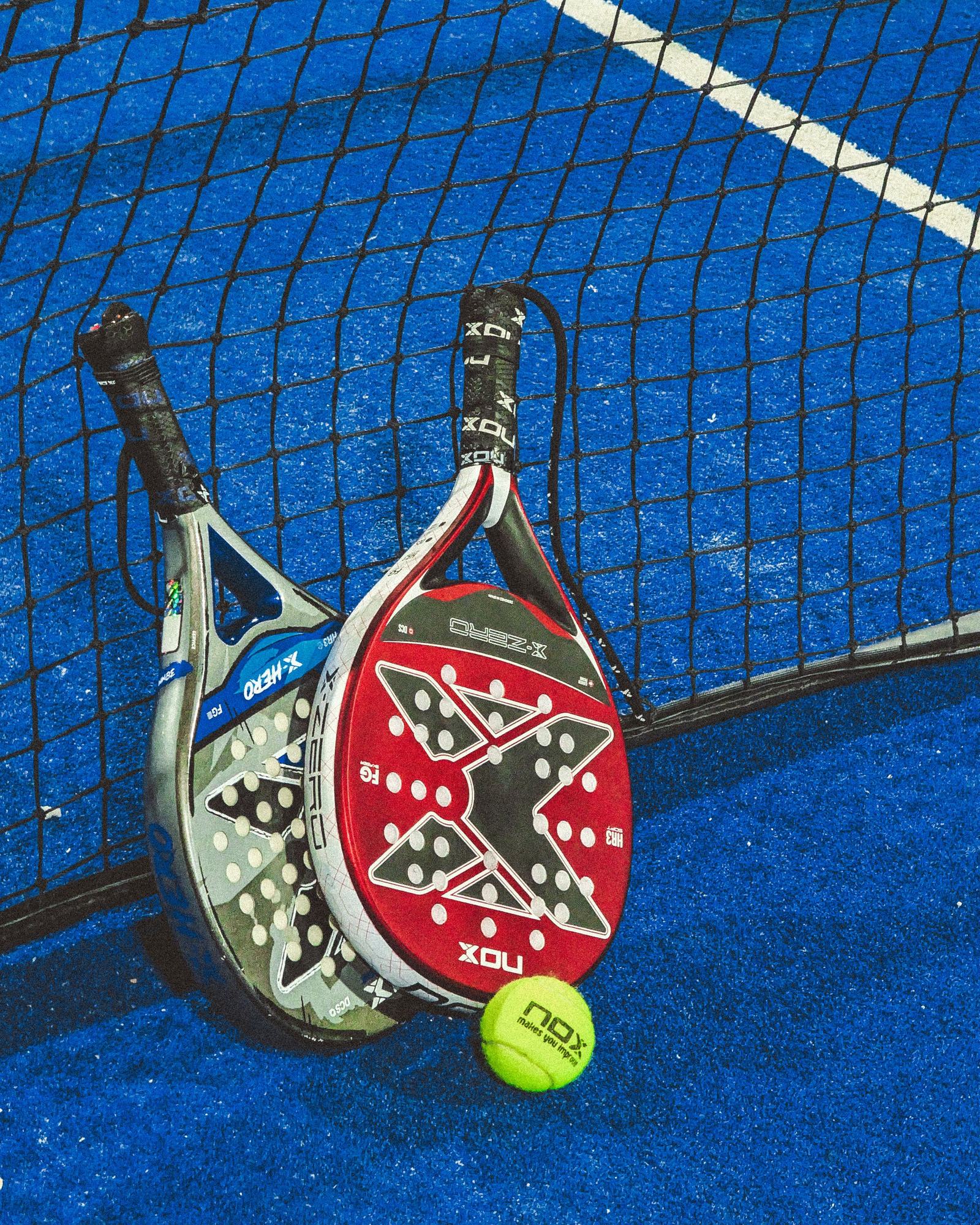 Two padel rackets and a ball resting against the net
